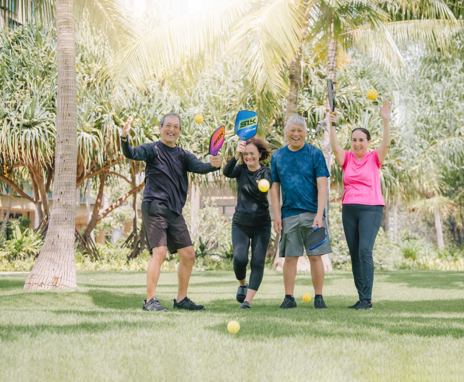 Group of pickleball players cheering with paddles raised under palm trees